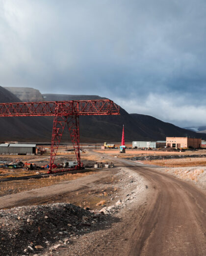 Exploring the abandoned industrial landscape of Pyramiden in Svalbard under dramatic clouds The remnants of an old mining settlement in Pyramiden, Svalbard, reveal a desolate industrial atmosphere. Rusting cranes and buildings stand against a backdrop of harsh, sweeping clouds.