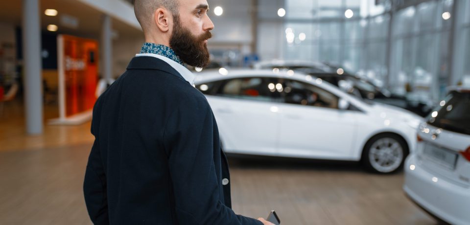 Smiling man poses in car dealership. Customer in new vehicle showroom, male person buying automobile, auto dealer business