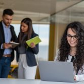 Confident attractive young business woman with tablet in hands in modern office start up office in front of working business team