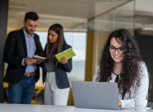 Confident attractive young business woman with tablet in hands in modern office start up office in front of working business team