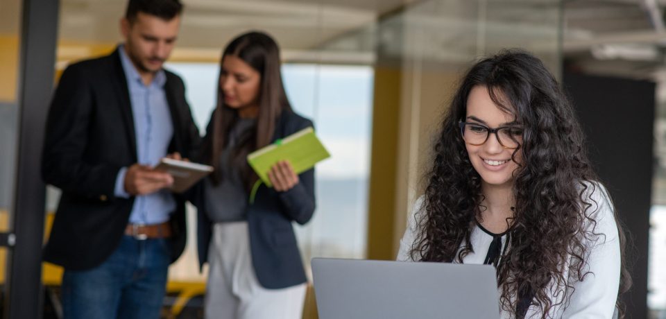 Confident attractive young business woman with tablet in hands in modern office start up office in front of working business team